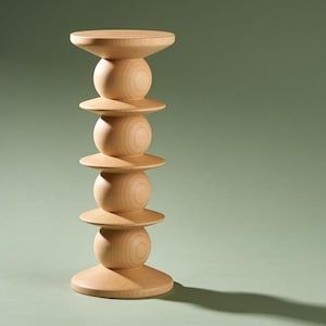 May include: A light-colored wooden pedestal stand featuring a vertical stack of four spherical shapes separated by flat, circular discs. The structure has a wide, circular base and a matching flat circular top, showcasing a natural wood grain finish.