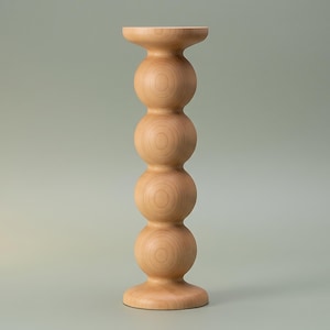 May include: A light-coloured wooden candle holder featuring a vertical stack of four smooth, spherical shapes. The object has a flat, circular base at the bottom and a matching flat, circular top platform designed to hold a single candle securely.