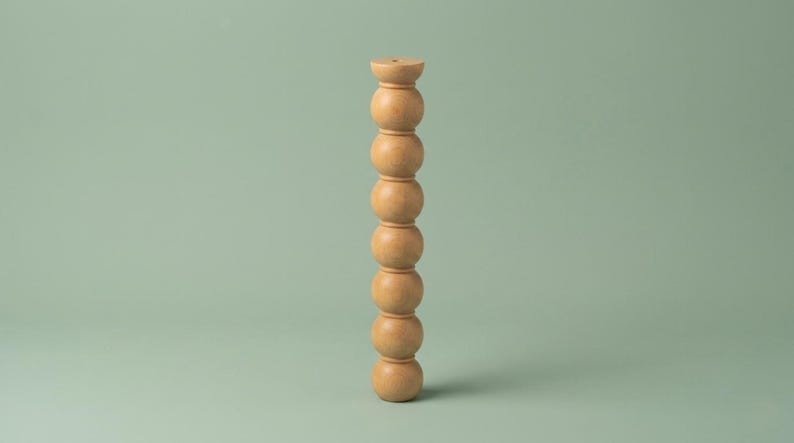 Op de afbeelding: Een verticale houten zuil bestaande uit een stapel van zeven gladde, bolvormige kralen. Het object heeft een lichtbruine afwerking met een natuurlijke houtnerf en een platte, ronde bovenkant met een klein, gecentreerd gat in het midden.