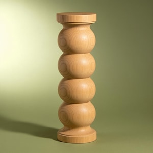 May include: A cylindrical wooden pedestal featuring a light tan natural wood grain finish. The structure consists of four stacked, rounded bulbous sections with a flat circular top and a matching flat circular base, creating a vertical column.