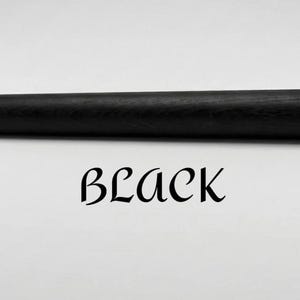 Op de afbeelding: Een massieve zwarte cilindrische staaf met een zichtbare houtnerftextuur, horizontaal in het kader geplaatst. Onder de staaf staat het woord BLACK gedrukt in een gestileerd, decoratief zwart schreeflettertype op een witte achtergrond.