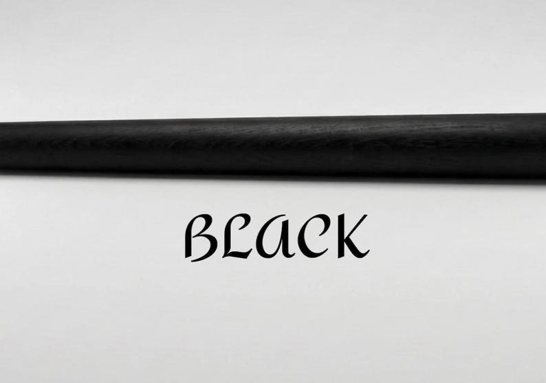 Op de afbeelding: Een massieve zwarte cilindrische staaf met een zichtbare houtnerftextuur, horizontaal in het kader geplaatst. Onder de staaf staat het woord BLACK gedrukt in een gestileerd, decoratief zwart schreeflettertype op een witte achtergrond.