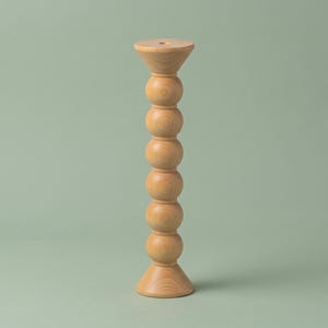 May include: A light brown wooden candle holder featuring a tall, vertical column composed of six stacked spherical shapes. The object has a flared, circular base and a matching flared top platform with a small central hole for a candle.