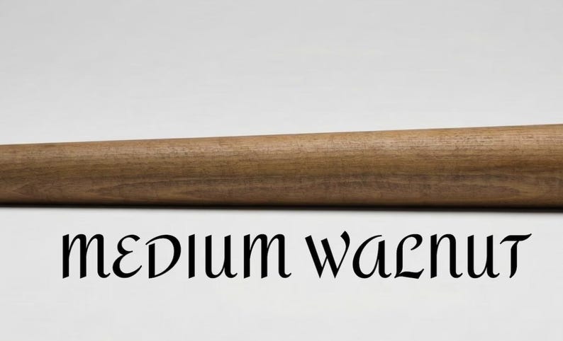 Op de afbeelding: Een cilindervormige houten staaf met een gladde, middelbruine walnootafwerking. De houtnerf is zichtbaar over de gehele lengte van het object. Onder de staaf staat de tekst "MEDIUM WALNUT" gedrukt in een zwart, gestileerd schreeflettertype.