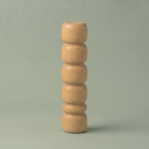 May include: A vertical wooden sculpture composed of five stacked, rounded, light-brown cylindrical segments. The object features a smooth, polished finish with visible natural wood grain patterns throughout its entire length, standing upright.
