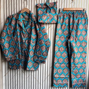 May include: A matching pajama set in a vibrant teal color with a repeating floral pattern in pink and brown. The set includes a button-down shirt, pants, and a drawstring bag. White piping trims the edges of the shirt and pants.