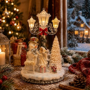 Könnte beinhalten: Eine dekorative Weihnachts-Tischfigur mit einer zentralen Straßenlaterne mit drei beleuchteten Laternen, einem Schneemann, einem kleinen Reh, einer Engelsfigur, einem strukturierten weißen Baum und einem Hasen auf einem verschneiten Sockel.