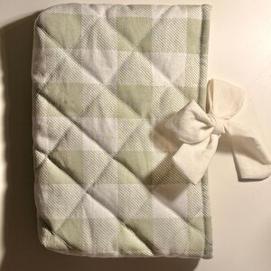 Op de afbeelding: Een gewatteerde notitieboekhoes met een groen-wit ruitpatroon, afgesloten met een crèmekleurige strik. De hoes heeft een ruitvormig quiltpatroon en is gemaakt van een zachte, getextureerde stof. De strik zit aan de zijkant.