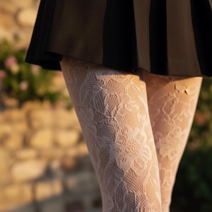 May include: Close-up of white lace tights with a floral pattern. The tights are worn with a black skirt. The image is taken outdoors with a blurred background of a brick wall and greenery.