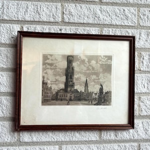 Pode incluir: Uma gravura emoldurada a preto e branco de uma paisagem urbana europeia. A gravura apresenta uma torre alta e outros edifícios, com pessoas em primeiro plano. A moldura é castanha escura e a gravura está protegida por vidro.