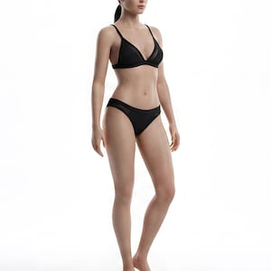 May include: A full-body shot of a person wearing a black lingerie set. The set includes a triangle-style bra and matching bikini bottoms. The person is standing on a clear, circular platform against a white background.