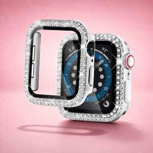 Pode incluir: Uma capa protetora para smartwatch em tom prateado, incrustada com strass transparentes e brilhantes. A capa apresenta recortes precisos para os botões laterais e a coroa digital. Uma segunda capa idêntica está posicionada à frente.