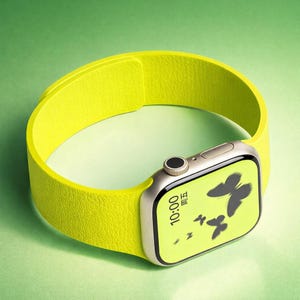 Op de afbeelding: Een smartwatch met een felgele band en een zilverkleurige behuizing. De wijzerplaat toont vlinders en de tijd, 10:00 uur. De band heeft een getextureerde uitstraling.