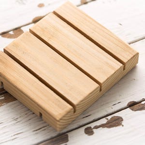 May include: A wooden soap dish with four grooves to hold bars of soap. The dish is made of light brown wood and has a natural finish.