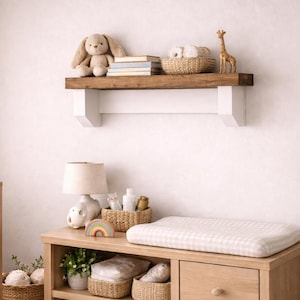 May include: A light wood baby nursery with a crib, changing table, and shelf. The changing table has a white pad and storage baskets. A stuffed bunny and giraffe are on the shelf. A potted plant is in the corner.