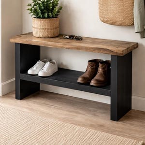 Pode incluir: Banqueta de madeira com base e prateleira pretas, com tênis brancos e botas marrons. Uma cesta de vime com uma planta em cima. Espelho redondo e tapeçaria de parede tecida.