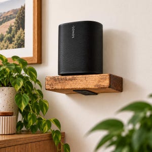 Könnte beinhalten: Ein schwarzer Sonos-Smart-Lautsprecher mit zylindrischer Form und Netzgitter, platziert auf einem rechteckigen, rustikalen Wandregal aus Holz. Der Lautsprecher zeigt das weiße Sonos-Logo vertikal ausgerichtet auf der Vorderseite.