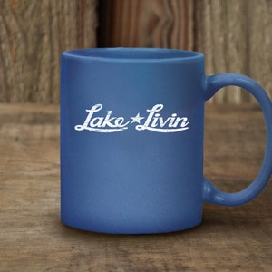 May include: A blue ceramic coffee mug with a white design that says "Lake Livin'" with a star between the words.