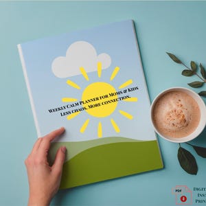 May include: A weekly planner for moms and kids with a blue sky and sun design. The planner has the text "WEEKLY CALM PLANNER FOR MOMS & KIDS LESS CHAOS. MORE CONNECTION." A cup of coffee and a sprig of leaves are next to the planner.