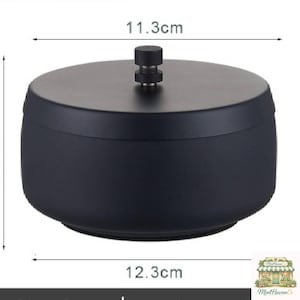 May include: A black, round container with a lid and a small handle. The container is 12.3 cm in diameter and 11.3 cm wide. The lid has a small, cylindrical handle. The container is likely used for storage or display.