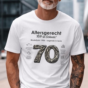 May include: White t-shirt with the text "Altersgerecht TOP in Schuss!" and the number 70 composed of mechanical parts. The shirt also features small illustrations and the text "Modelljahr 1956 - Legende in Serie."