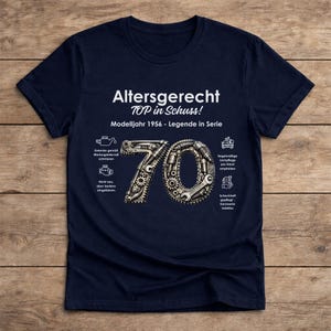 May include: Navy blue t-shirt with the text "Altersgerecht TOP in Schuss! Modelljahr 1956 - Legende in Serie". The number 70 is designed with gears and tools. Additional text and icons are also present.