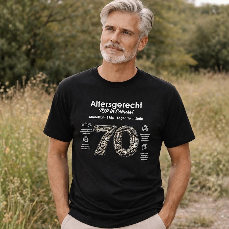 May include: Black t-shirt with white text that reads "Altersgerecht TOP in Schuss! Modelljahr 1956 - Legende in Serie." The number "70" is designed with gears and mechanical parts. The shirt is worn by a person.
