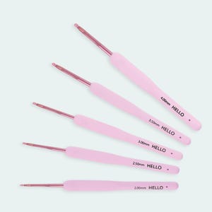May include: Five pink crochet hooks with metallic tips are arranged diagonally. Each hook has a different size, indicated by the text: 2.00mm, 2.50mm, 3.00mm, 3.50mm, and 4.00mm. The word "HELLO" is printed on each hook.