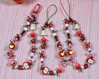 May include: Three beaded keychains with apple, star, and mushroom charms. The keychains feature red, white, and pearl-colored beads. The charms include red apples, white stars, and red mushroom beads. The keychains are adorned with red and green leaves.