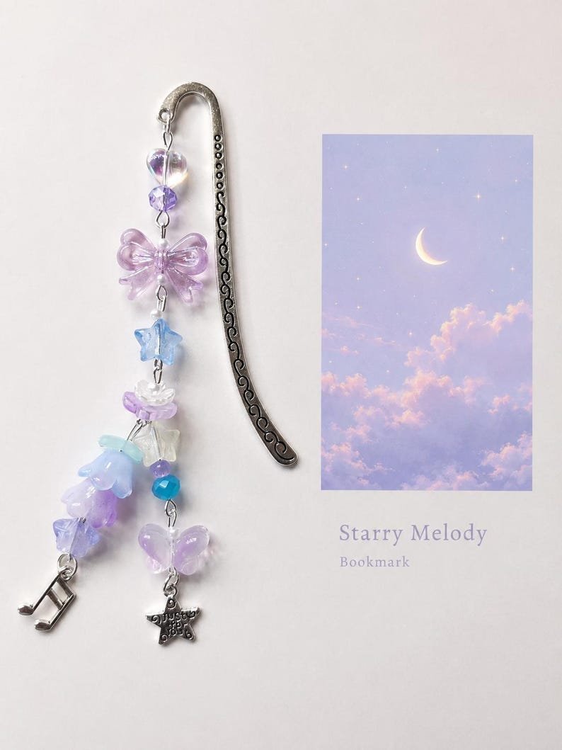 May include: A silver metal bookmark with a curved, patterned spine, adorned with a dangling charm strand featuring purple and blue beads, translucent butterfly shapes, star-shaped beads, flower-shaped beads, a music note charm, and a star charm.