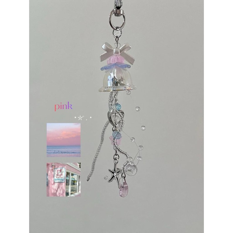 May include: A pink and silver keychain featuring a clear bell-shaped charm, adorned with a bow, beads, and a starfish pendant. The word "pink" is written in pink. Includes small images of a pink sunset and a pink building.
