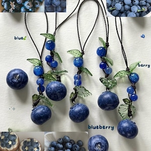 May include: A collection of blueberry-themed items. The image features several blueberry pendants with glass leaves, along with close-up shots of fresh blueberries and blueberry pastries. The word "blue" and "blueberry" are written in the image.
