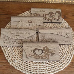 Könnte beinhalten: Fünf rechteckige Holzhüllen mit lasergravierten Motiven. Die Designs enthalten Texte wie Happy Wedding, Happy Wedding Day, John und Sophia sowie Abbildungen von Herzen, Eheringen, einem Auto und einem sich umarmenden Paar.