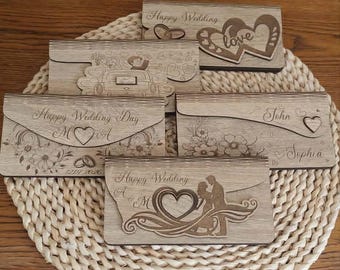 May include: Five rectangular wooden envelopes with laser-engraved designs. The designs include text such as Happy Wedding, Happy Wedding Day, John, and Sophia, along with illustrations of hearts, wedding rings, a car, and a couple in an embrace.