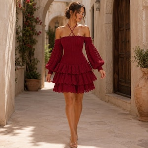 May include: A burgundy off-the-shoulder dress with long sleeves and a tiered skirt. The dress features a halter neckline and a fitted bodice. The sleeves are long and have a balloon shape. The dress is made of a textured knit fabric.