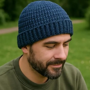 May include: A dark blue beanie crafted with a textured crochet stitch pattern. The hat features a thick, ribbed brim that sits snugly around the head, providing a consistent, uniform appearance with a deep navy color throughout the entire piece.