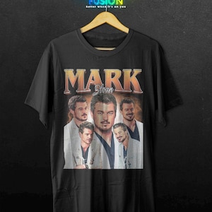May include: Black t-shirt featuring a collage of images of Mark Sloan with the name "MARK Sloan" in an orange and white vintage style. The shirt has the text "FASHION FUSION" at the top.