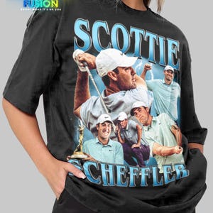 Puede incluir: Camiseta unisex negra con un gráfico del golfista Scottie Scheffler. El diseño incluye el nombre "SCOTTIE SCHEFFLER" en letras azules, junto con imágenes del golfista. La camiseta también tiene el logo "FASHION FUSION".