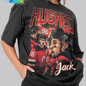 K&ouml;nnte beinhalten: Schwarzes Unisex-T-Shirt mit einer Grafik eines Eishockeyspielers, dem Namen "HUGHES" in Rot und der Spielernummer "86". Der Name "Jack" ist ebenfalls abgebildet. Das Fashion Fusion-Logo ist oben zu sehen.