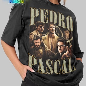 以下が含まれることがあります： ペドロ・パスカルのヴィンテージスタイルのグラフィックと「PEDRO PASCAL」の文字が入った黒のユニセックスTシャツ。 シャツはクルーネックと半袖です。 ファッションフュージョンのロゴが左上にあります。