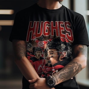 K&ouml;nnte beinhalten: Schwarzes T-Shirt mit dem Namen "HUGHES" in roten Blockbuchstaben. Das Shirt zeigt eine Grafik eines Eishockeyspielers in einem schwarzen Helm und einem roten Trikot. Das Logo "Fashion Fusion" befindet sich oben links.