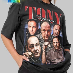 Puede incluir: Camiseta negra con un collage de imágenes de Tony Soprano y el texto "TONY Soprano" en rojo y blanco. La camiseta tiene un logotipo de Fashion Fusion en la esquina superior izquierda. La camiseta es de estilo unisex.