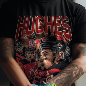K&ouml;nnte beinhalten: Schwarzes T-Shirt mit einem Hockey-Design. Es zeigt den Namen "HUGHES" in Rot und eine Collage von Hockeyspielern. Das Shirt zeigt auch den Text "FASHION FUSION" in einem farbenfrohen Farbverlauf.