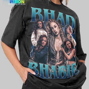 May include: Black unisex t-shirt featuring a graphic of multiple women with the text "BHAD BHABIE" in blue. The shirt has short sleeves and a crew neck. The Fashion Fusion logo is in the upper left corner.