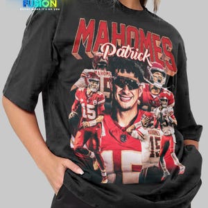 May include: Black unisex t-shirt featuring a graphic of Patrick Mahomes in a red and white football uniform. The shirt has the text "MAHOMES" and "Patrick" in red. The shirt also has the "FASHION FUSION" logo.