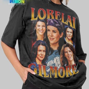 May include: Black unisex t-shirt featuring a graphic of the character Lorelai Gilmore from the TV show Gilmore Girls. The design includes multiple images of the character and the text "LORELAI GILMORE" in a vintage style. The shirt has the Fashion Fusion logo.