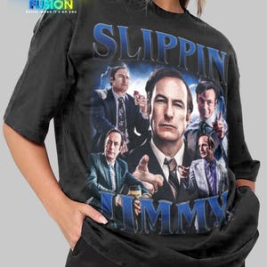 Peut inclure: T-shirt noir avec un graphisme d'un homme en costume et le texte "SLIPPIN JIMMY" en bleu. Le design est de style vintage avec plusieurs images de l'homme. Le logo Fashion Fusion est dans le coin supérieur gauche.