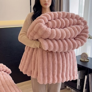May include: A plush, dusty pink blanket featuring a distinct ribbed, textured surface. The fabric has a soft, faux-fur appearance with vertical channels running throughout the material, creating a consistent, repeating pattern across the entire surface.
