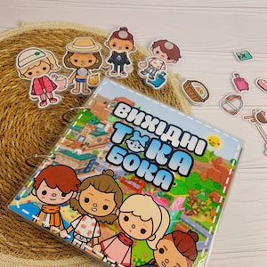 May include: A square, ring-bound activity book featuring a colourful cartoon scene with four characters on the cover and the text "ВИХІДНІ ТОКА БОКА". Several small, die-cut paper character figures and travel-themed accessories are arranged nearby.