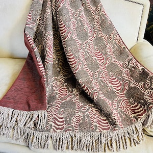 May include: A red and cream throw blanket with a brown tiger print. The blanket has a fringe border.